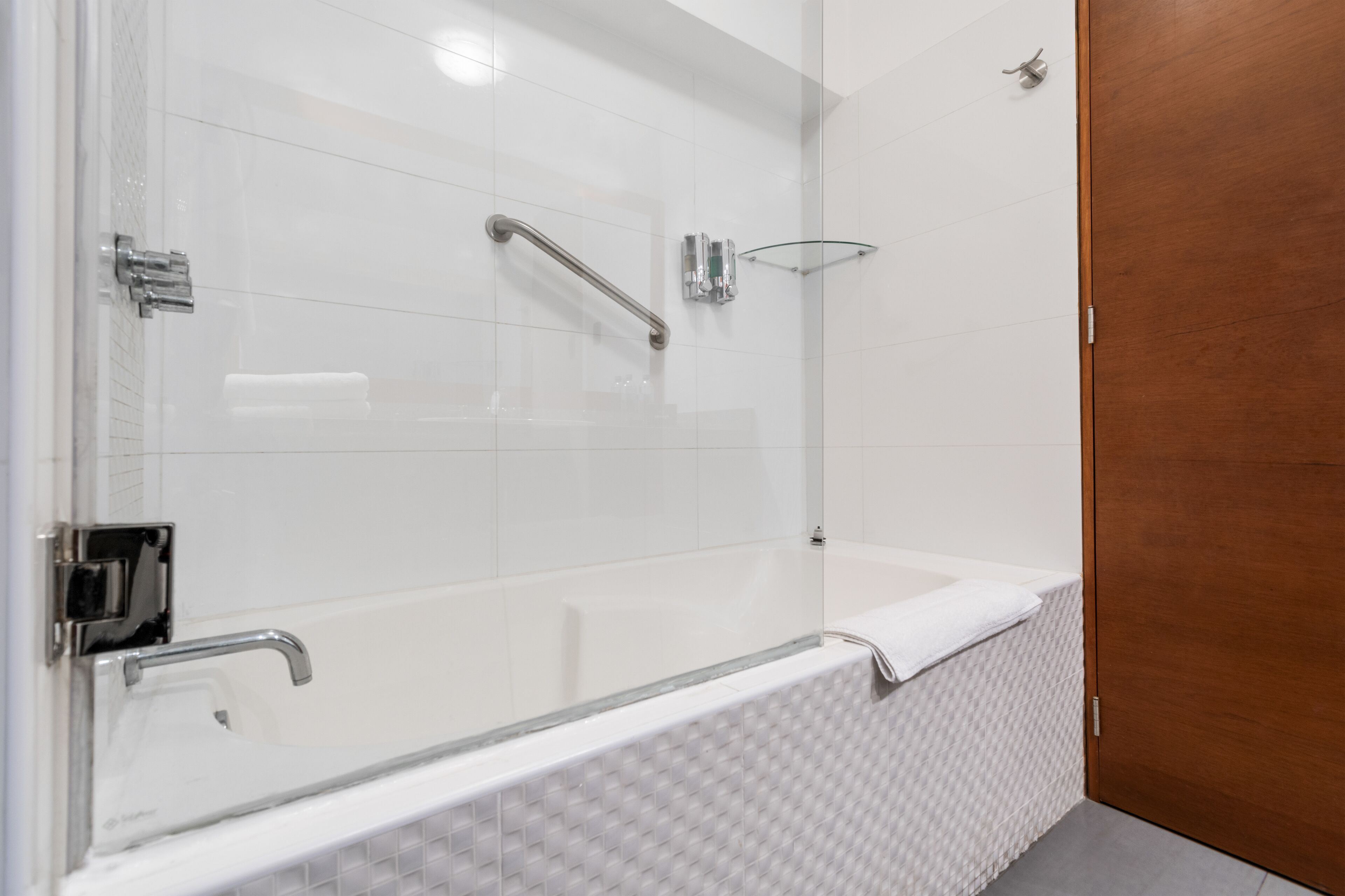 A modern bathroom with a glass-enclosed shower, a white bathtub, and a wooden door.