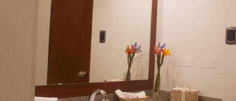 Un baño con lavamanos, espejo y dos jarrones con flores.