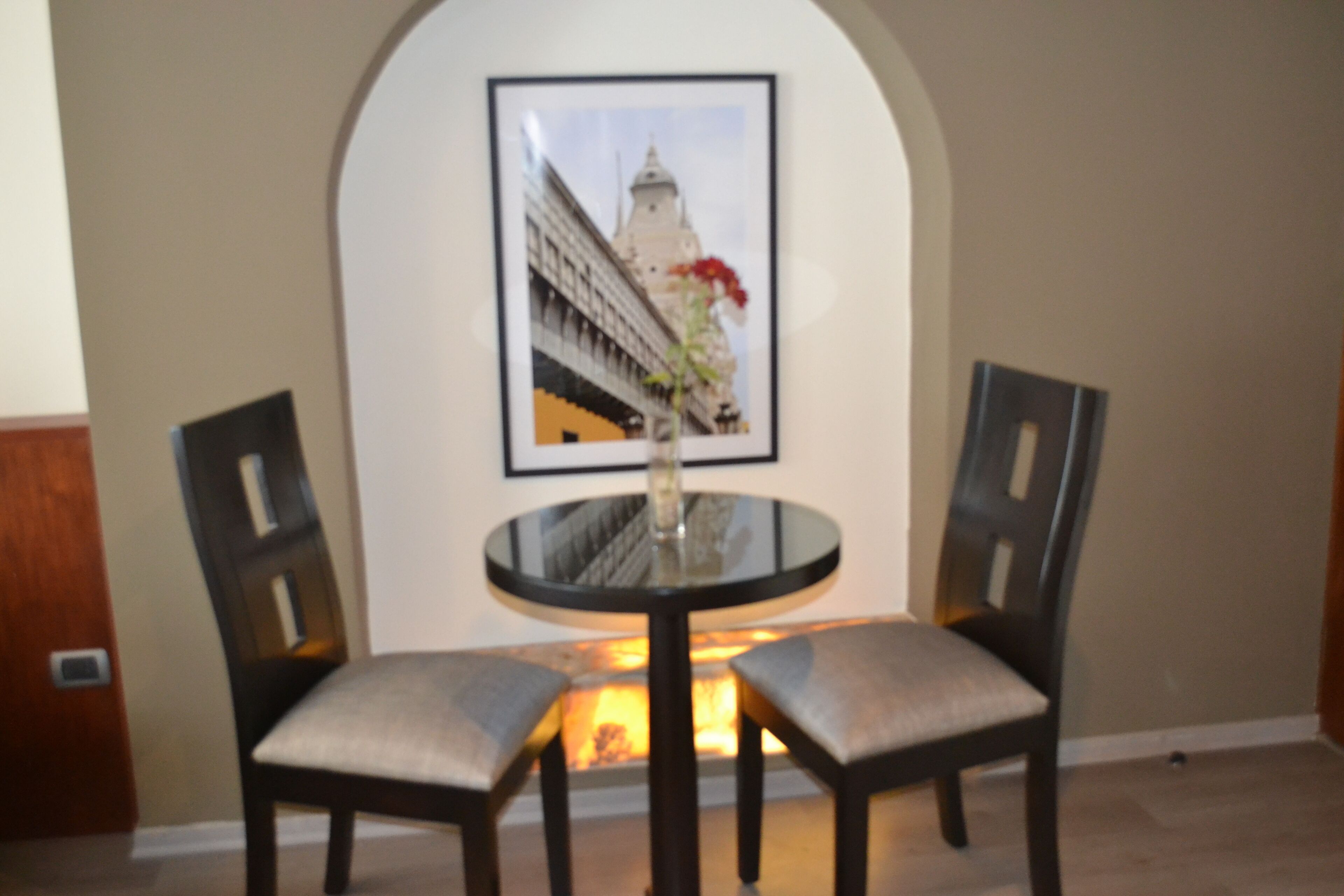Un comedor con una mesa redonda, dos sillas y un cuadro con una imagen de un edificio en la pared.