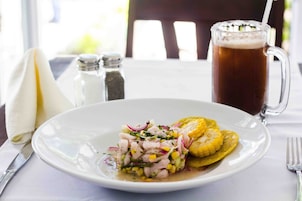 Ein Teller Ceviche mit Mais und roten Zwiebeln, ein Bierglas und ein Salzstreuer auf einem Tisch.