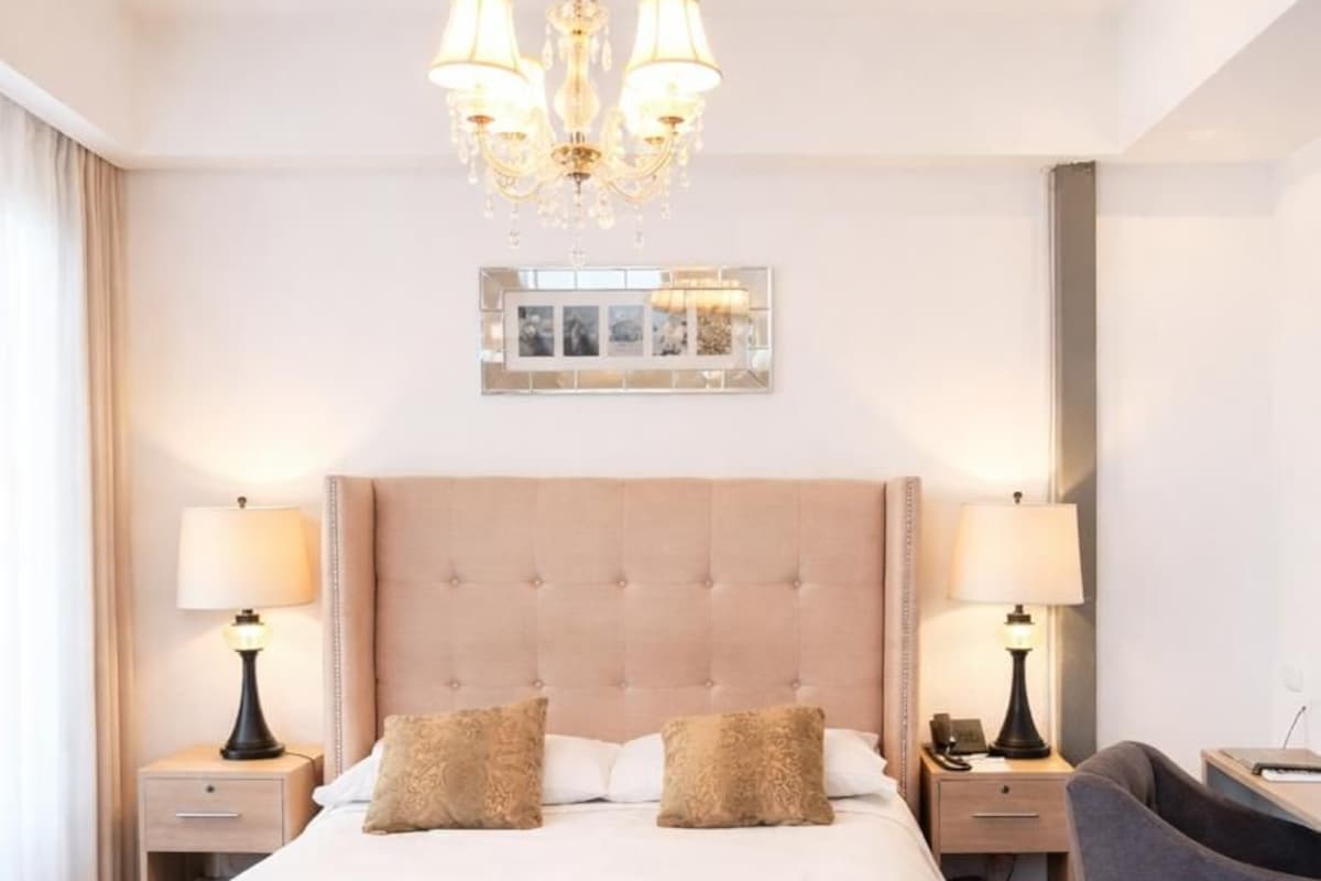 Une chambre d’hôtel avec un grand lit, deux tables de chevet avec des lampes, un lustre et un miroir au mur.