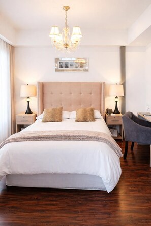 Un cuarto de hotel con una cama grande, dos mesitas de noche con lámparas, un candelabro y un espejo en la pared.
