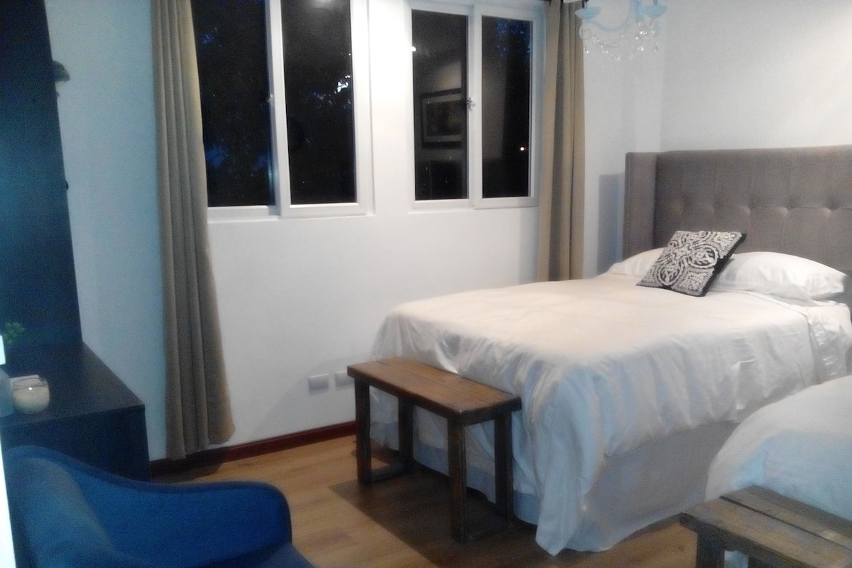 Un dormitorio con cama, una mesita, una silla y una ventana.