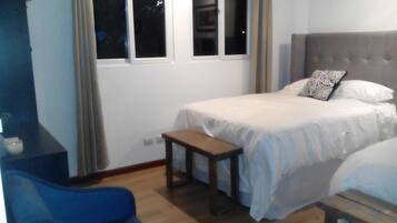 Quarto com cama, uma mesa pequena, uma cadeira e janela.