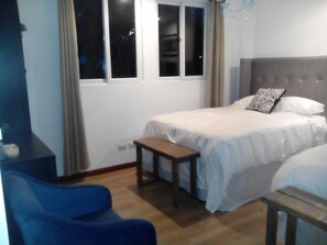 Un dormitorio con cama, una mesita, una silla y una ventana.