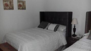 Una cama doble con cabecera oscura, una mesita de noche con lámpara y dos cuadros colgados en la pared.