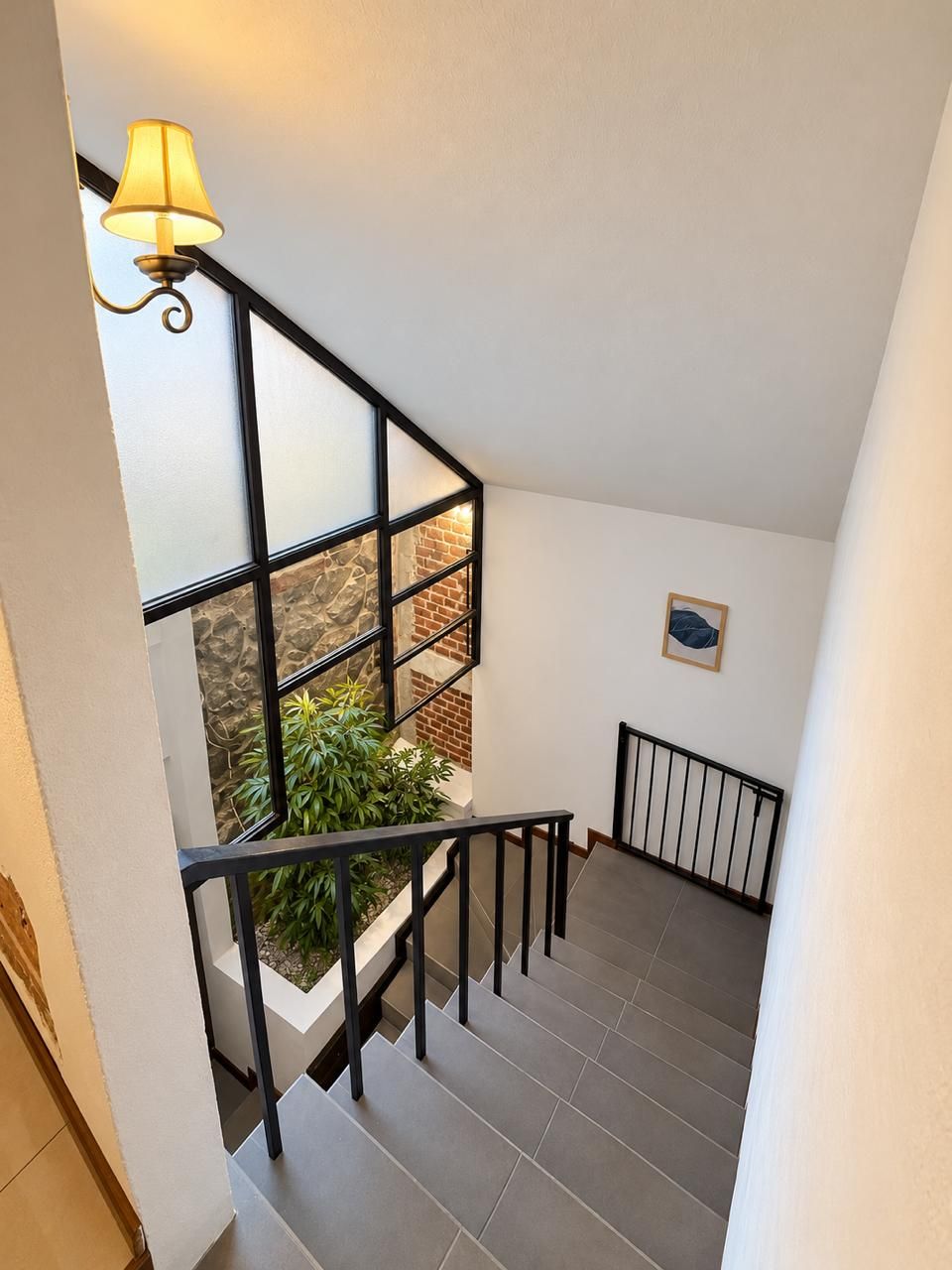 A staircase with a black railing, a wall-mounted light fixture, and a framed picture.