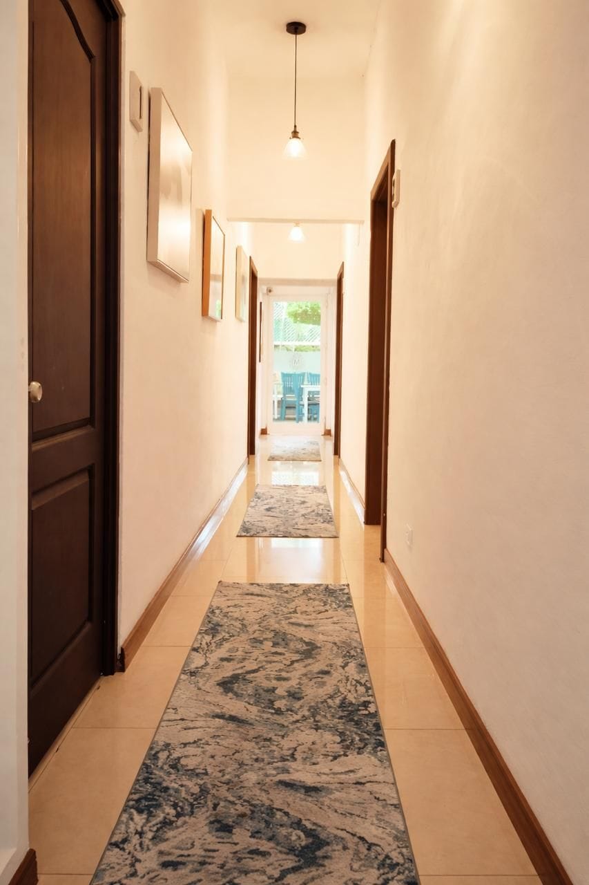 A hallway with a patterned rug, framed pictures on the wall, and a door on the left.