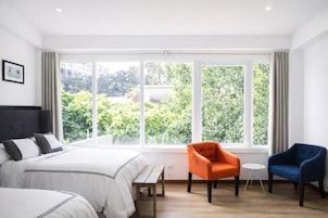 A hotel room with a large window, a bed, two chairs, and a small table.
