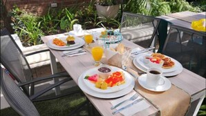 Una mesa para comer al aire libre dispuesta con alimentos de desayuno, incluyendo platos de comida, un vaso de jugo de naranja y una taza de café.