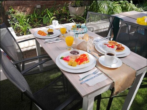 Ein Tisch im Freien mit Frühstücksleckereien, darunter Teller mit Speisen, ein Glas Orangensaft und eine Tasse Kaffee.