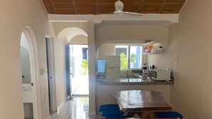 A spacious living area with a tiled floor, a wooden sofa with patterned cushions, a dining table, and a kitchen in the background. - Casa del Sol (Santa María Huatulco)