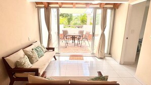 A room with a sofa, a coffee table, and a dining table with chairs. There is a sliding glass door leading to an outdoor patio area. - Casa del Sol (Santa María Huatulco)