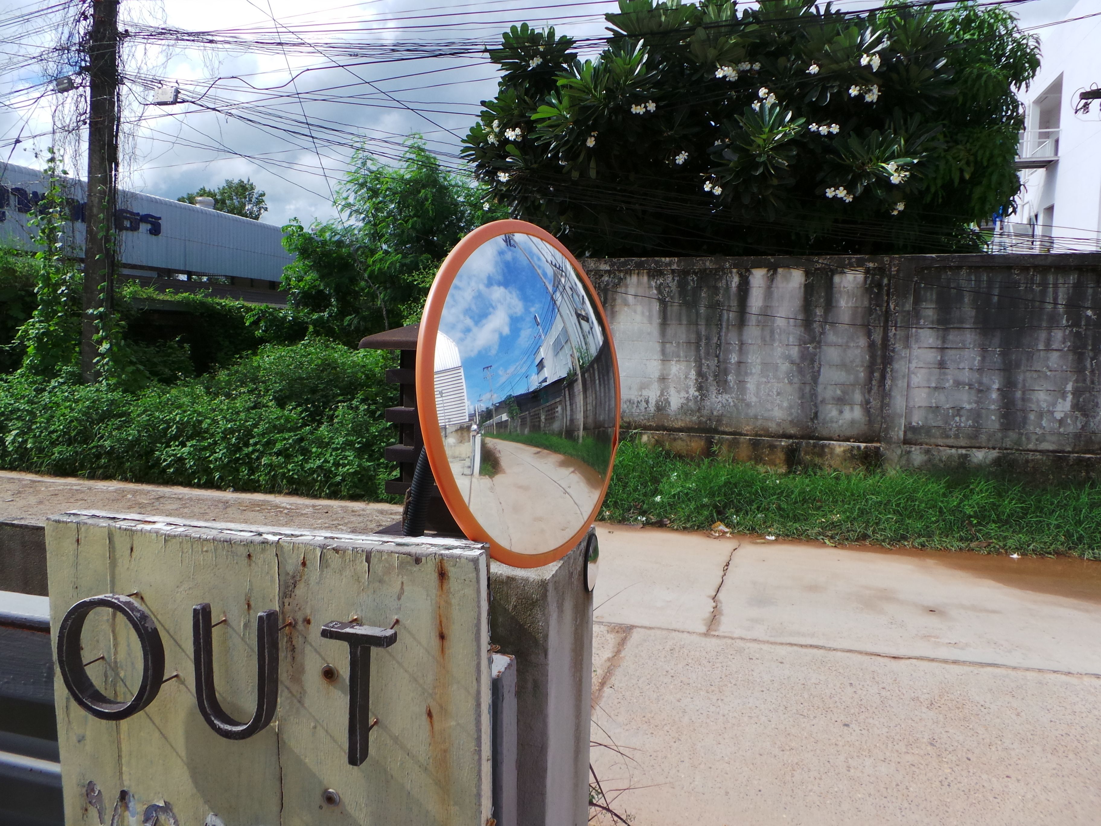 A road sign with the word "OUT" and a circular mirror reflecting a building and sky.
