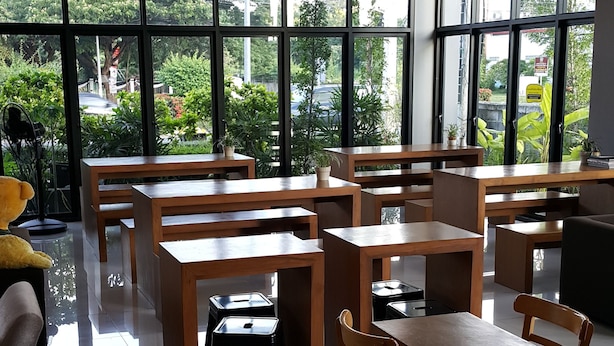 Amplio espacio interior con varias mesas y sillas de madera, y grandes ventanales que ofrecen vistas a la vegetación.