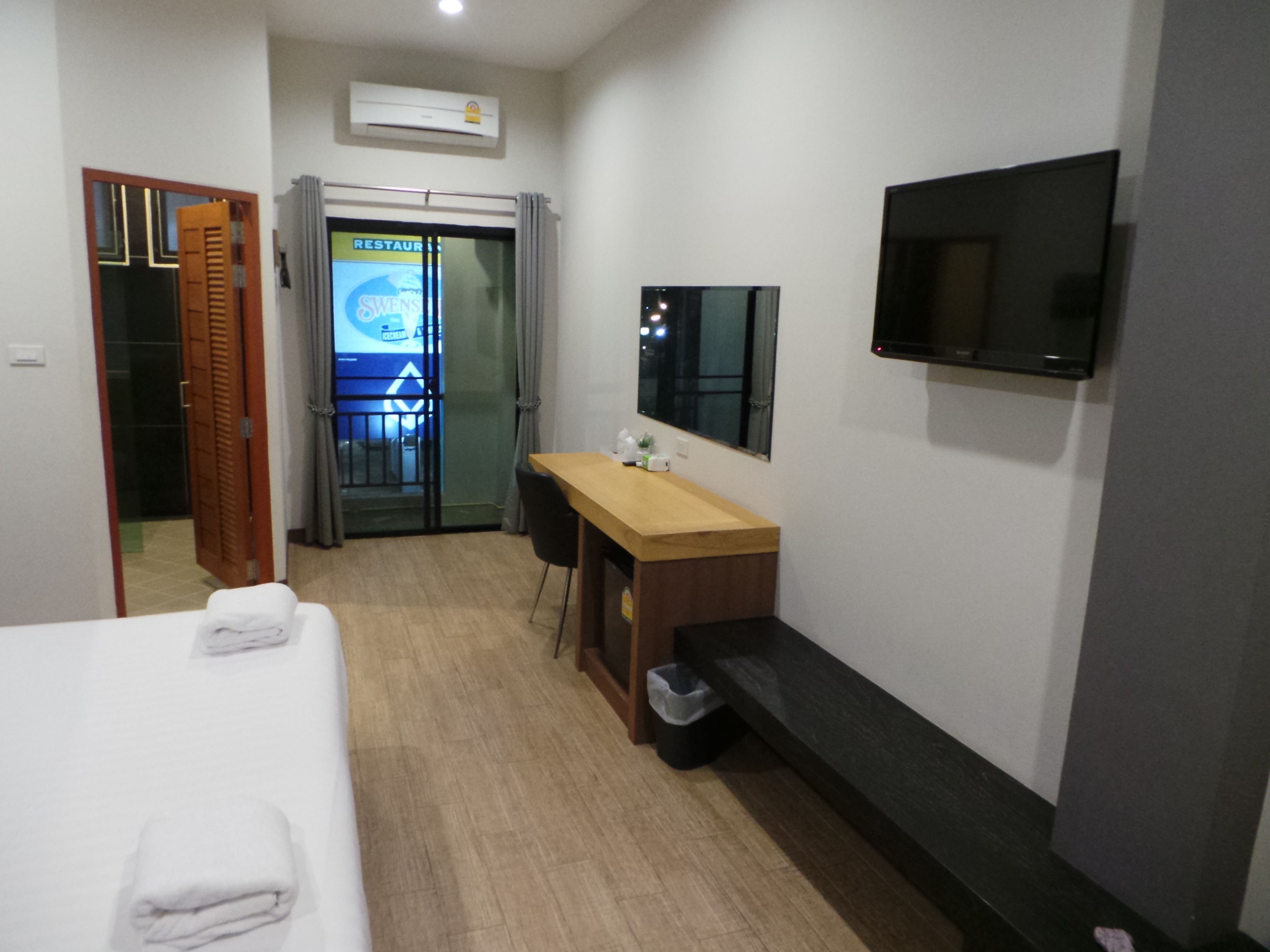 A hotel room with a bed, a wooden desk, a TV, and a trash bin.