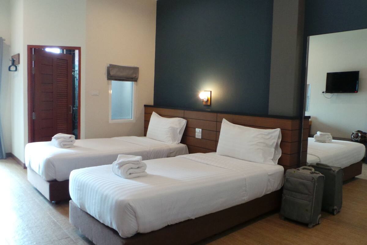 Une chambre d’hôtel avec deux lits, un grand miroir, une télévision et une valise.