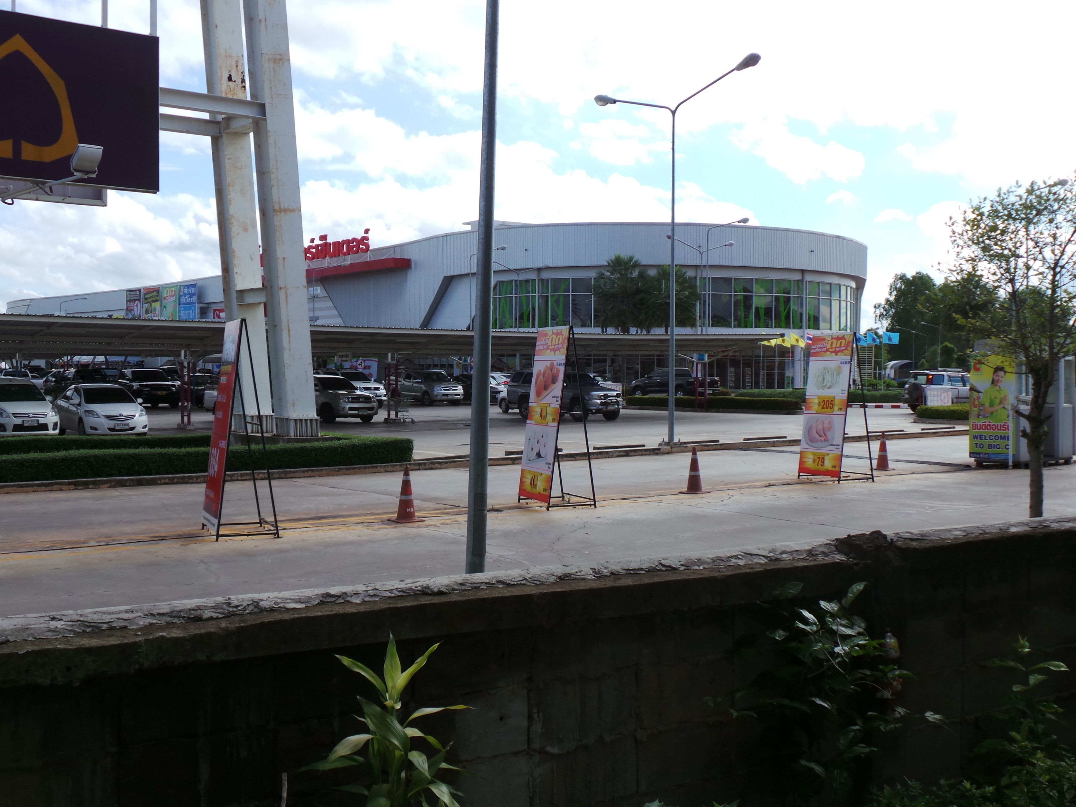 Un edificio moderno con fachada curva, múltiples accesos y un estacionamiento con varios coches.