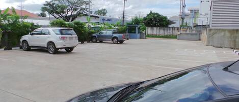 Un estacionamiento con varios coches, incluyendo un SUV blanco y una camioneta gris. Se ven edificios y árboles al fondo.