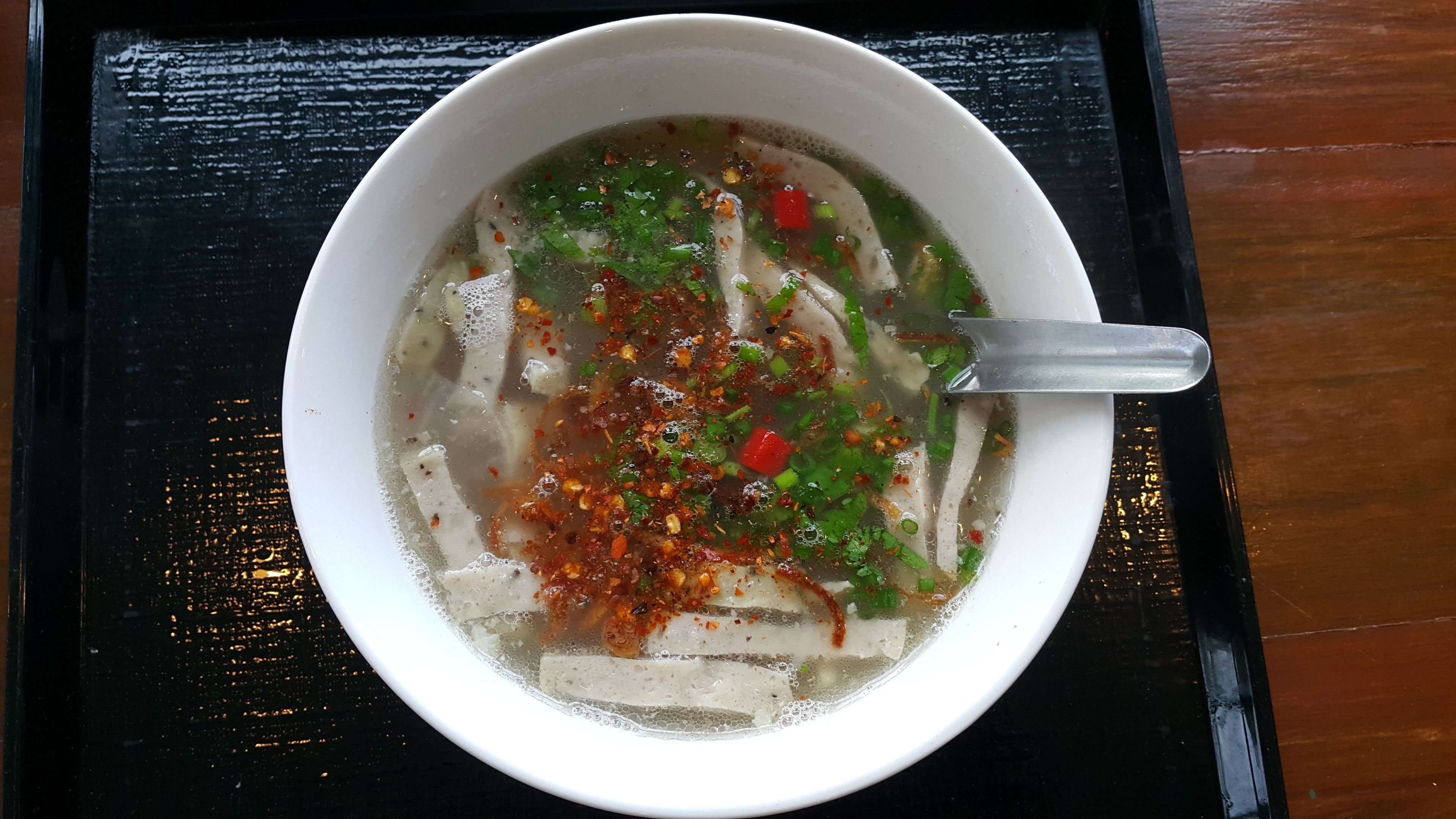 A bowl of soup with noodles, garnished with herbs and spices.