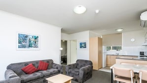 A modern living room with a grey sofa, a small table, and a kitchen area with a microwave and sink.