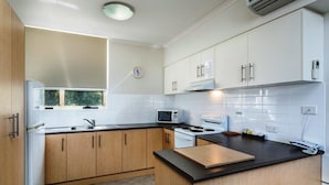 A modern kitchen with white cabinets, a black countertop, a microwave, a stove, and a clock on the wall.