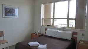 A hotel room with a bed, a nightstand, a chair, a window, and a framed picture on the wall.