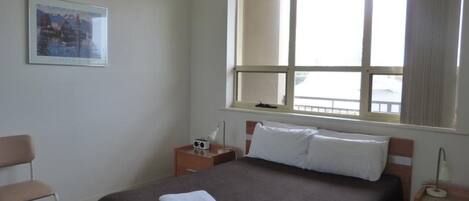A hotel room with a bed, a nightstand, a chair, a window, and a framed picture on the wall.