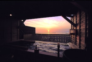 Una cabaña de madera con un jacuzzi y vistas de la puesta de sol sobre el agua.