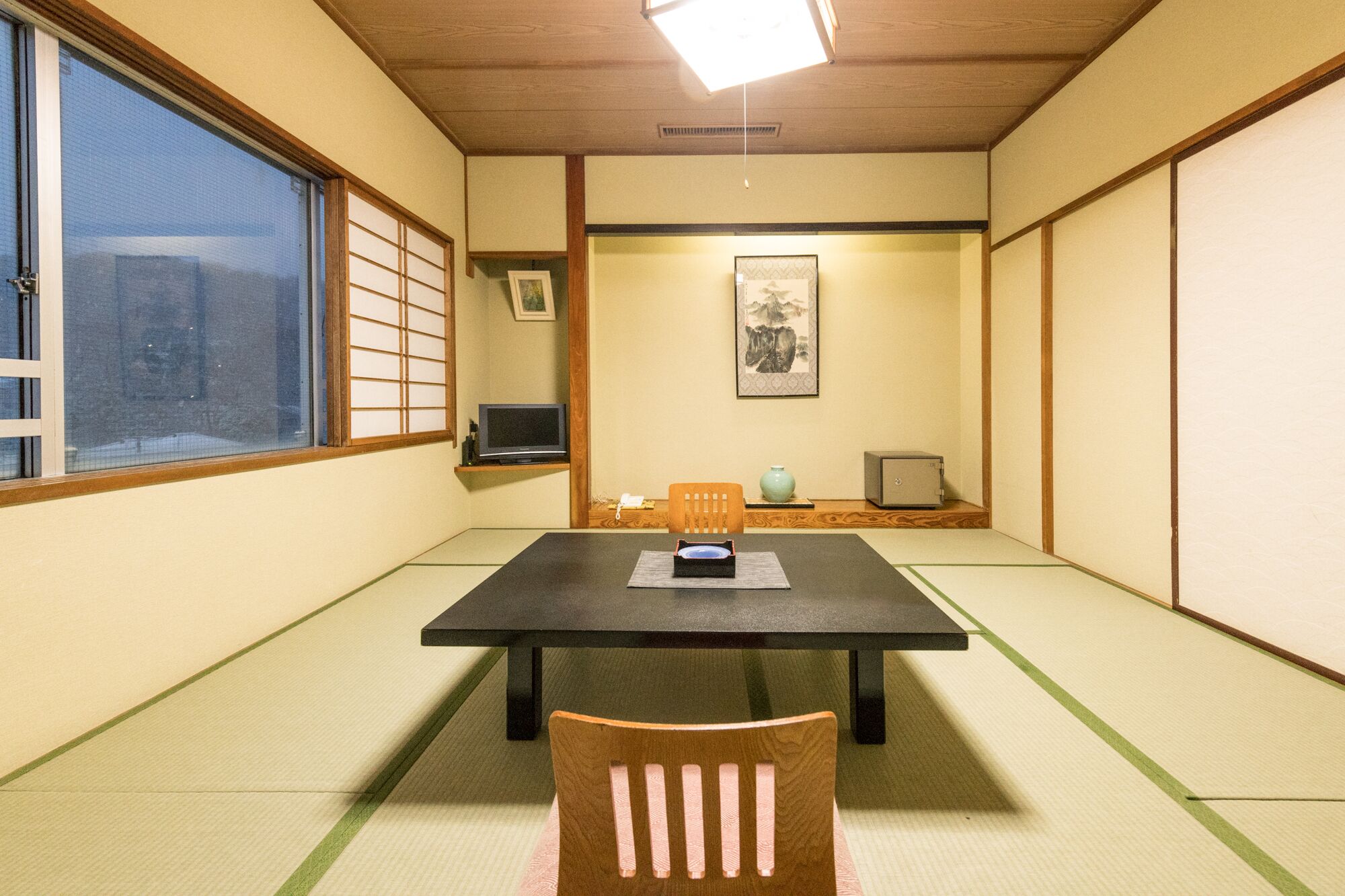 A traditional Japanese room with tatami flooring, a low table, and a wooden chair.