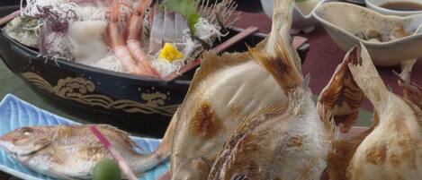 Diversos pratos de frutos do mar, incluindo peixe grelhado e camarão, servidos numa mesa com várias tigelas e pratos.