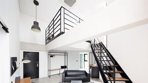 A spacious living area with a black sofa, wooden coffee table, and two wooden chairs. A black staircase with a metal railing leads to an upper level. - Gangneung Boutique Hotel Bombom (Gangneung)
