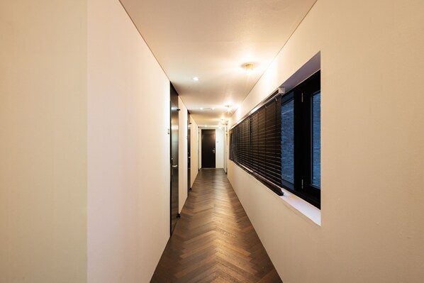 Un couloir étroit avec un plancher en bois, des murs blancs et une fenêtre équipée de stores.