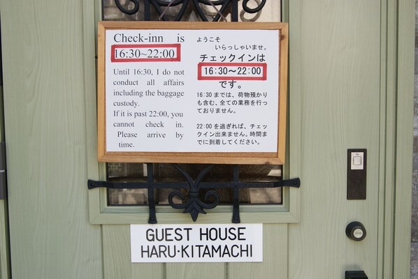 A sign indicating check-in times at a guest house in Haru-Kitamachi.