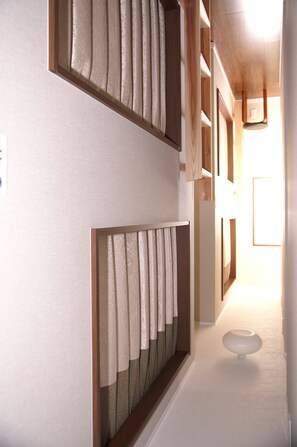 A hallway with a wooden floor, a white wall, and a white ceiling. There is a white object on the floor and a window with curtains.
