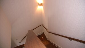 A wooden staircase with a handrail, a light fixture on the wall, and a door at the bottom.