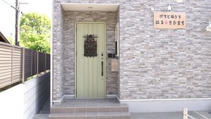 A building entrance with a green door, a stone wall, and a sign with Japanese text.