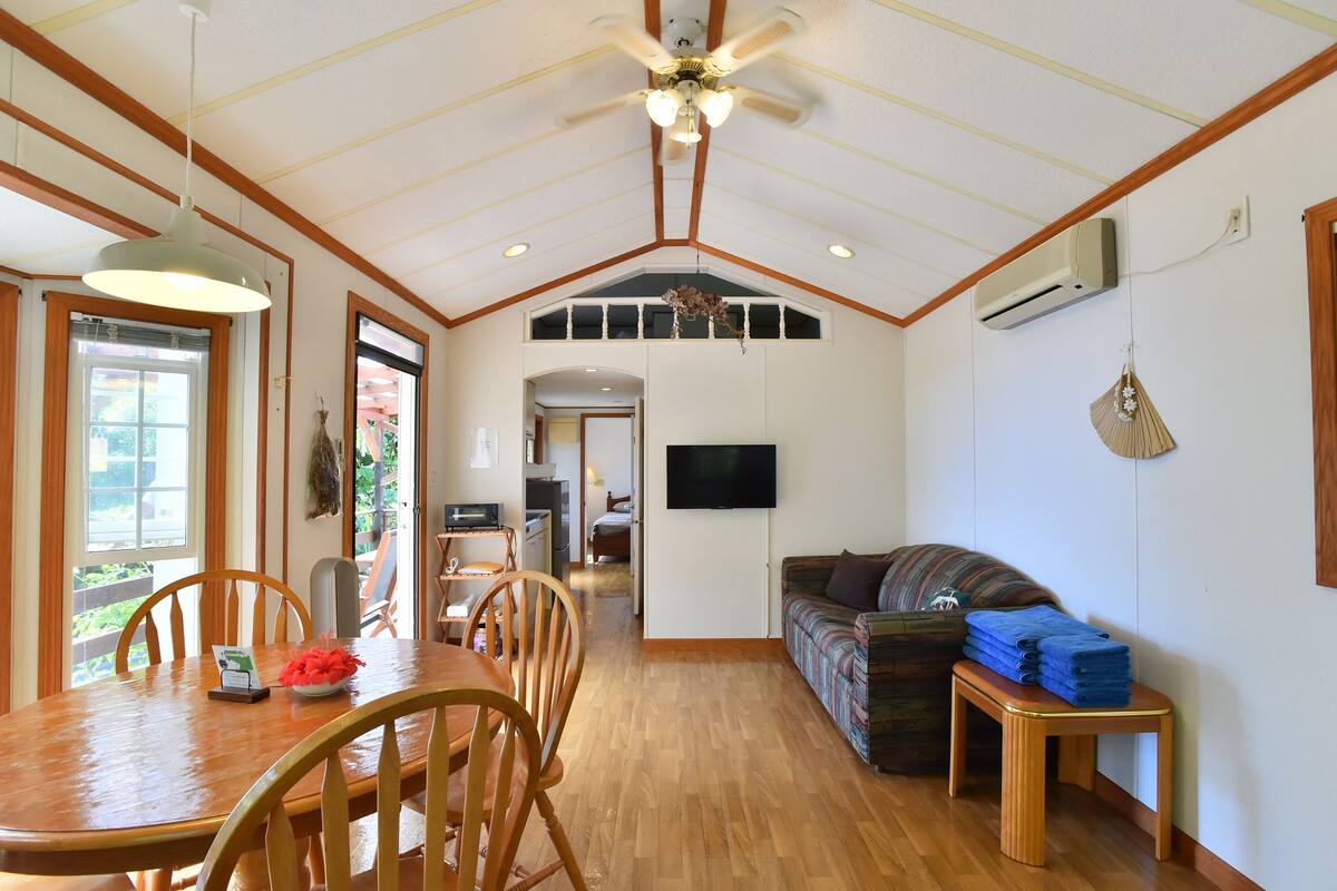 Uma sala de estar ampla com uma mesa de jantar de madeira, cadeiras, um sofá e um ventilador de teto.