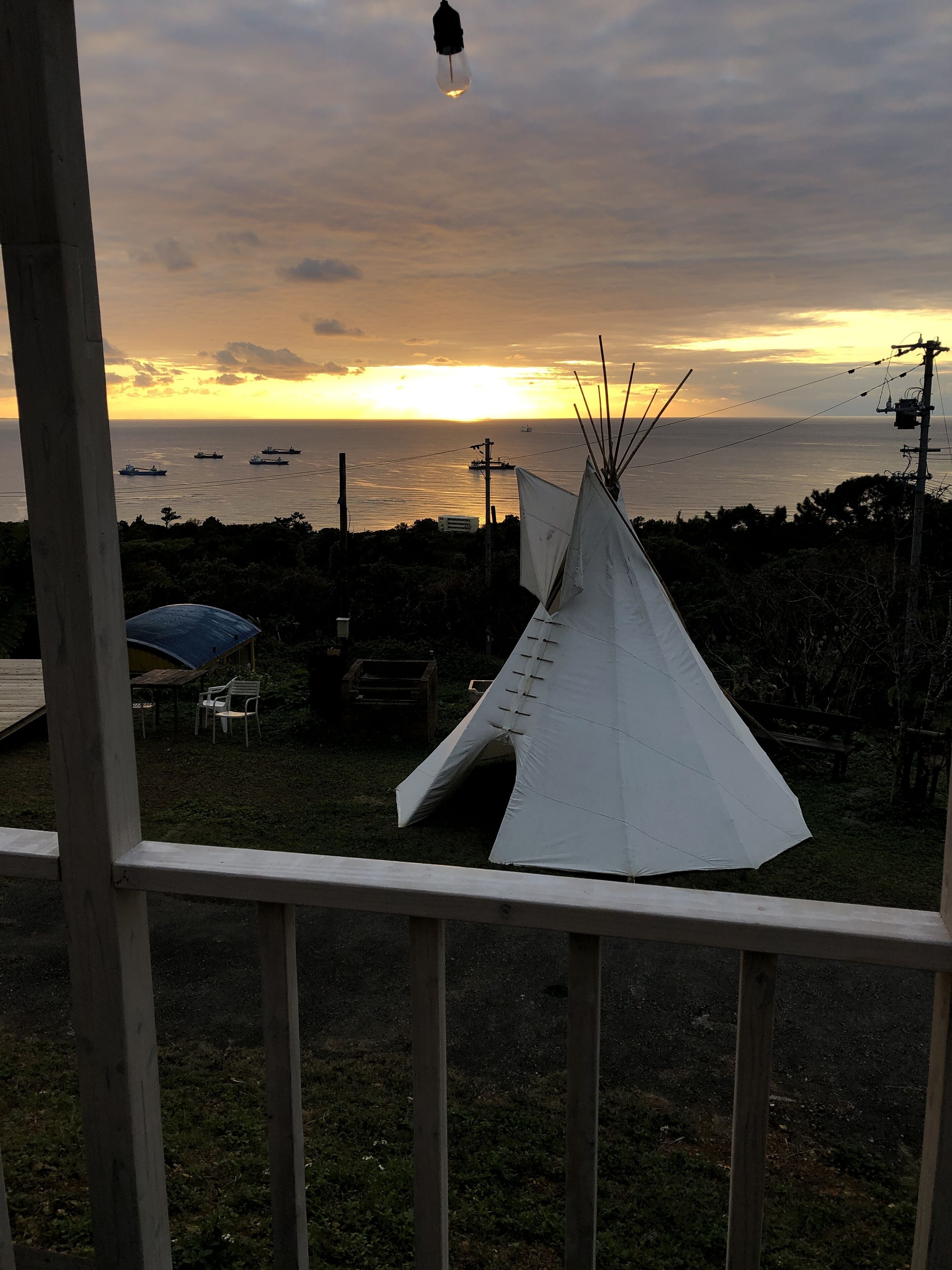 Vista de una estructura blanca tipo tipi en un área cubierta de pasto, con una terraza de madera al frente.