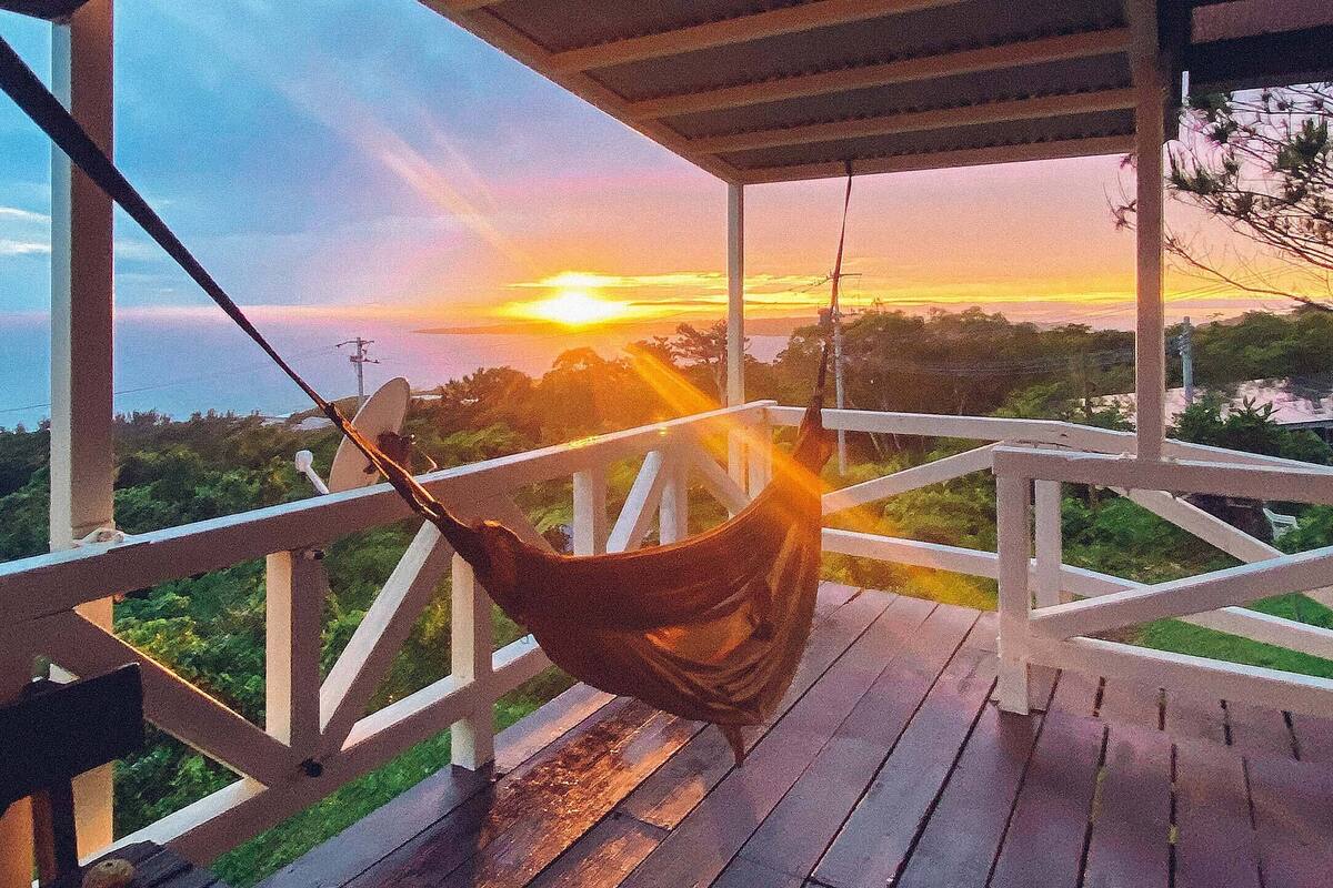Uma rede em um deck de madeira com vista para uma paisagem deslumbrante ao pôr do sol.