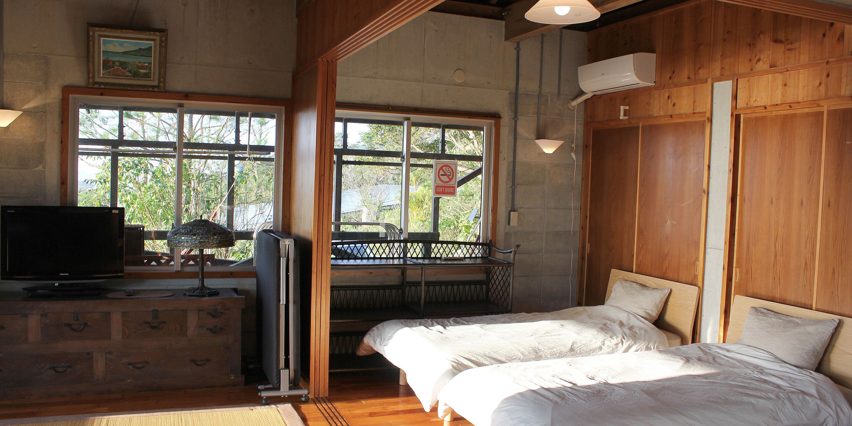 A room with a bed, a TV, a desk, and a window with a view of greenery.