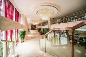 Een ruime, moderne hotel lobby met een marmeren vloer, grote kroonluchters en een glazen balustrade met uitzicht op een verdieping lager.