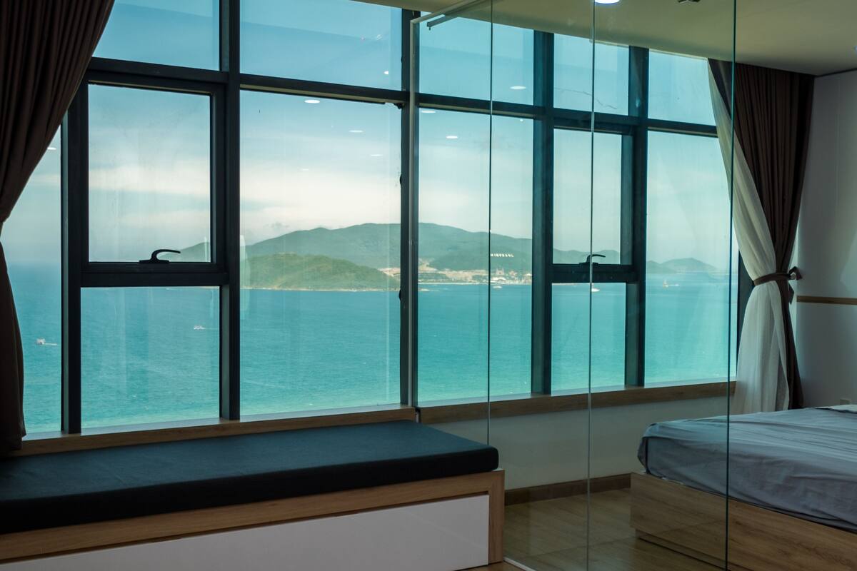 Ein Zimmer mit großem Fenster und Blick auf das Meer und ferne Berge.