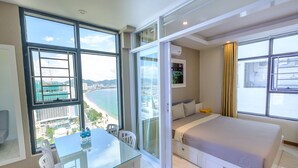 Habitación de hotel moderna con una cama grande, una mesa de comedor de vidrio y vistas a la ciudad y al mar.