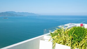 Vista al mar desde un balcón, con cielo despejado, mar tranquilo y montañas a lo lejos.