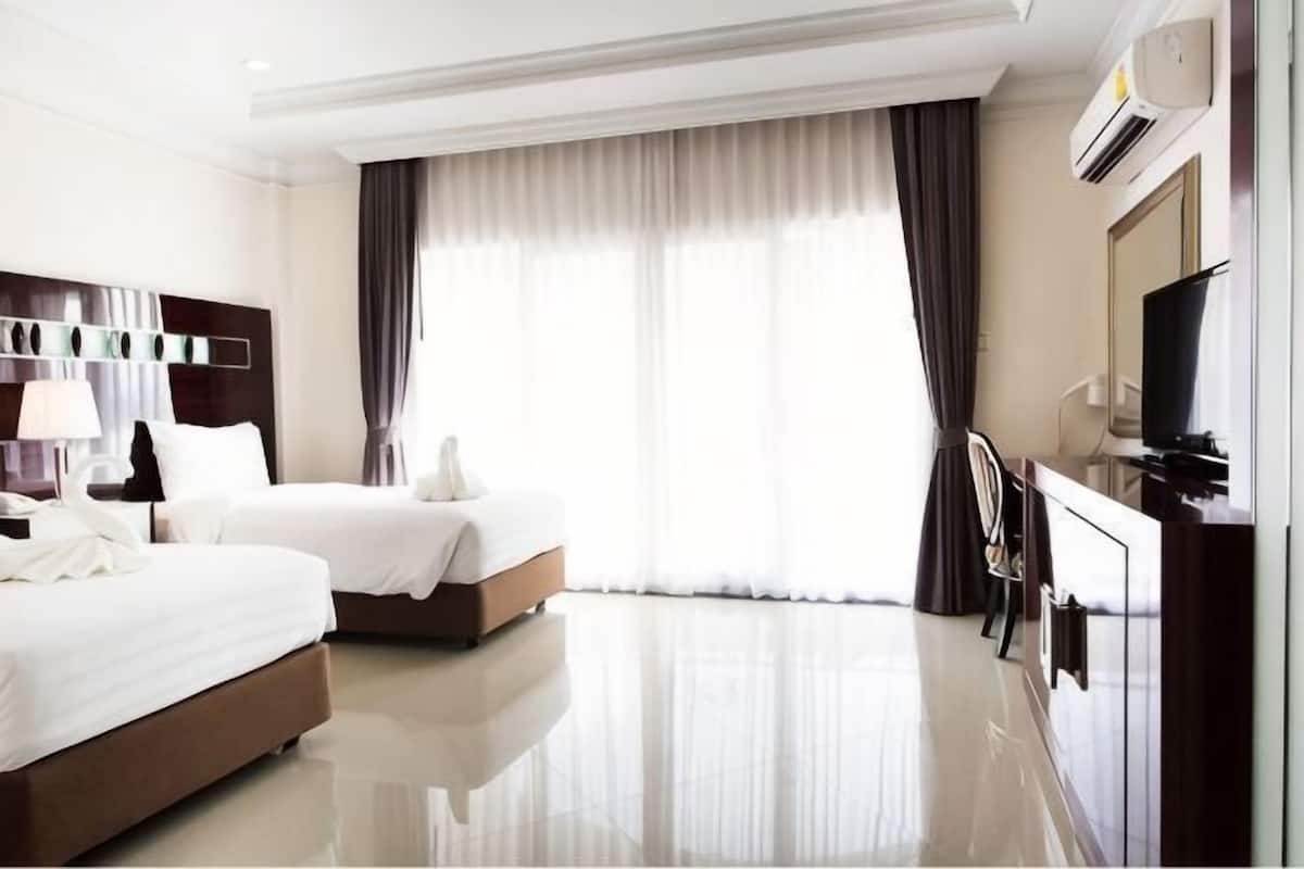 Quarto de hotel com duas camas, televisão, escrivaninha e uma janela grande com cortinas.
