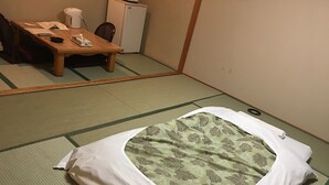 A tatami mat room with a bed, a small table with a kettle, and a refrigerator. - Hotel Crown Hills Kitami (Kitami)