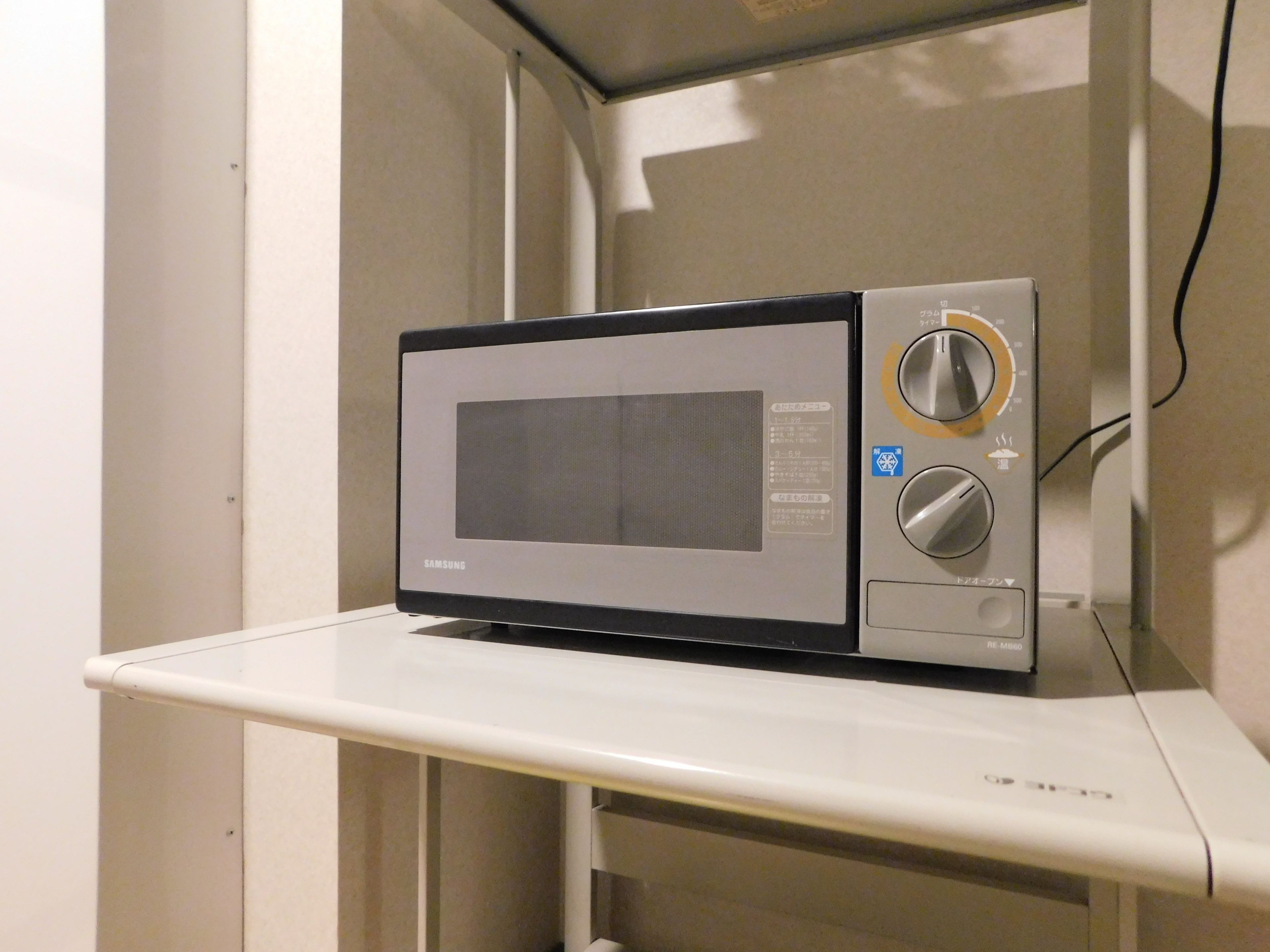 A microwave on a white shelf in a kitchen.