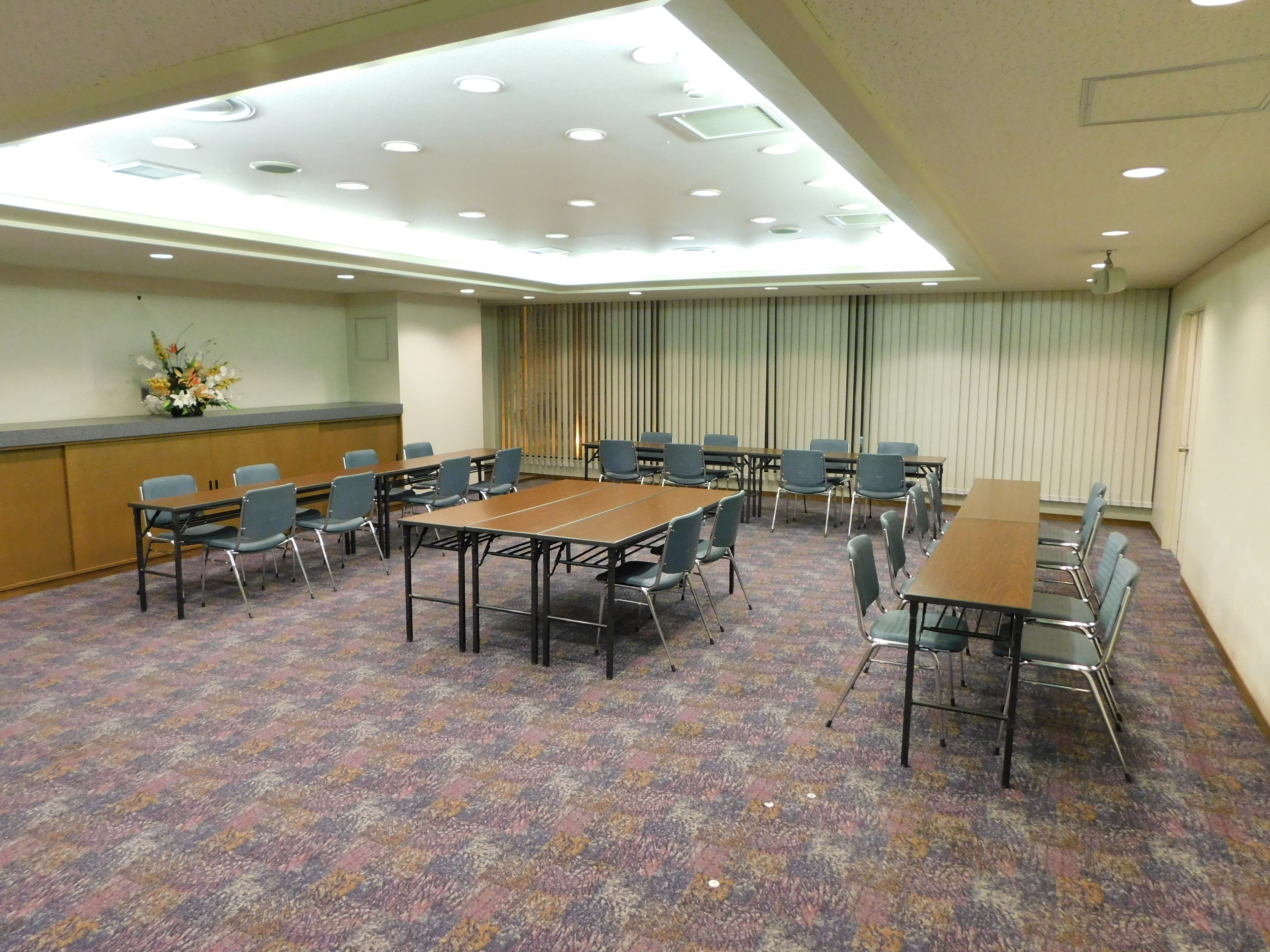 A conference room with a high ceiling, recessed lighting, and a patterned carpet.