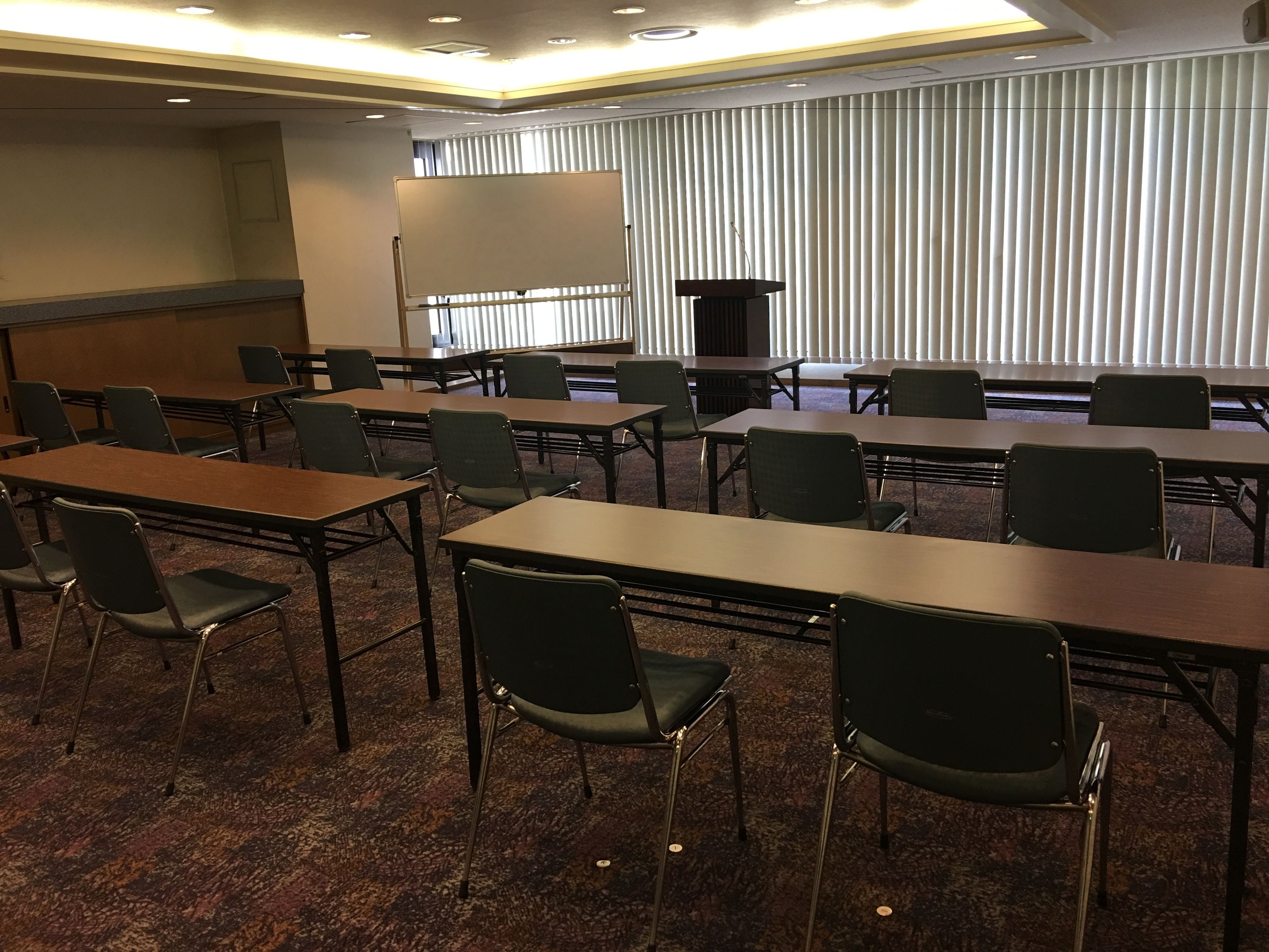 A conference room with multiple tables and chairs, a podium, and a projection screen.